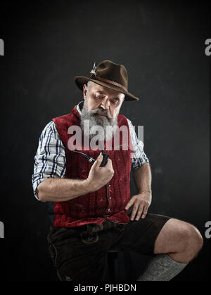 Dramatische Portrait von grauen Bärtigen älteren Mann in hat Tabak Pfeife. Blick auf die österreichischen und Tiroler, Bayerische alter Mann in nationaler Tracht im Retro-Stil. Stockfoto