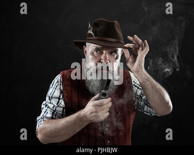 Dramatische Portrait von grauen Bärtigen älteren Mann in hat Tabak Pfeife. Blick auf die österreichischen und Tiroler, Bayerische alter Mann in nationaler Tracht im Retro-Stil. Stockfoto