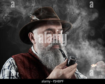 Dramatische Portrait von grauen Bärtigen älteren Mann in hat Tabak Pfeife. Blick auf die österreichischen und Tiroler, Bayerische alter Mann in nationaler Tracht im Retro-Stil. Stockfoto