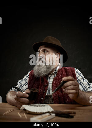 Die älteren bärtigen Mann am Tisch sitzen und das Verstopfen der Tabak in Rohr. Die männlichen Händen hautnah. Bayern. ein Mann in traditionelle bayerische oder Österreichische nationale Tracht gekleidet Stockfoto