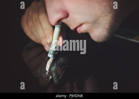 Junger Mann Kokainschnupfen mit Spiegel, Schreibtisch mit Reflexion auf schwarzem Hintergrund. Close-up Stockfoto