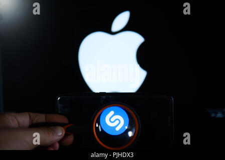 Shazam Logo ist durch ein Vergrößerungsglas auf ein Android Handy vor einem Computer Bildschirm mit Apple Logo gesehen. Stockfoto