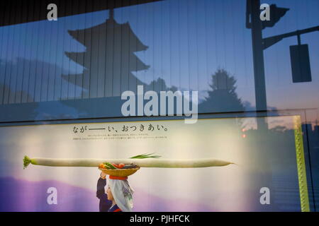 Japan, Kyoto, Dämmerung Blick auf eine Bank Fenster auf Omiya Avenue einschließlich ein Poster von einer Frau mit einem sehr langen daikon Rettich auf ihren Kopf und eine Reflexion von Toji Tempel des Holz- 5-stöckige Pagode (der höchste Holzturm in Japan) Stockfoto