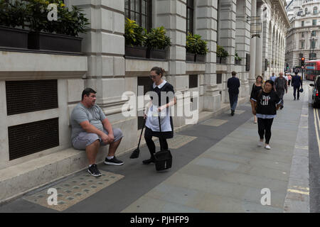 Ein weiblicher Angestellter kehrt Wurf von um die Füße ein übergewichtiger Mann sitzt außerhalb des Ned Hotel in Geflügel (Straße) in der Londoner City - der Capital District, am 3. September 2018 in London, England. Stockfoto