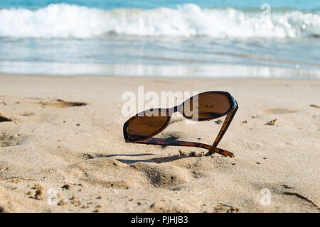 Sonnenbrille auf dem Sandstrand mit Blick auf das Meer im Hintergrund Stockfoto