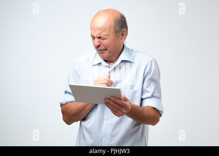 Senior kaukasischen der Mensch ist, was er auf einem Tablet Device sieht angewidert. Er ist auf der Suche Video im Internet ist und wirklich schockiert Stockfoto