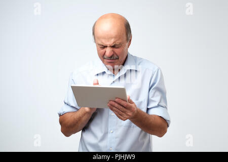 Senior kaukasischen der Mensch ist, was er auf einem Tablet Device sieht angewidert. Er ist auf der Suche Video im Internet ist und wirklich schockiert Stockfoto