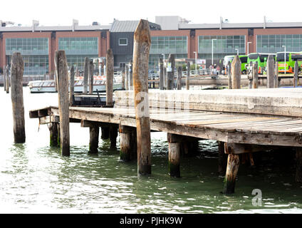 Hölzerne Seebrücke in den Stapel unterstützt Touristische in Venedig einzuschiffen, im Hintergrund drei grüne Busse mit einer Gruppe von Menschen und Boote Stockfoto