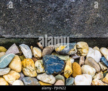 Unterschiedliche Farben der Kieselsteine gegen ein blauer Granit Wand Garten Dekoration Hintergrund Textur Stockfoto
