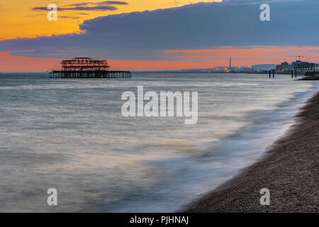 Der Strand in Brighton, England, nach Sonnenuntergang mit der Ruine der alten Pier in der Rückseite Stockfoto