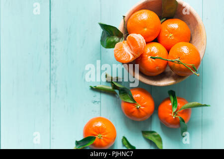 Reifen Mandarinen mit Blättern in einer rustikalen Holzmöbeln Schüssel auf eine blau türkis Tabelle. Selektiver Fokus Stockfoto