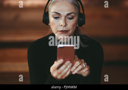 Closeup Portrait von Senior Geschäftsfrau hören Musik von smart phone. Wunderschöne reife Frau mit Kopfhörer Musik hören. Stockfoto