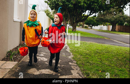 Identische Zwillingsschwestern in halloween kostüm mit halloween Eimer laufen auf dem Bürgersteig. Halloween Kinder Süßes oder Saures. Stockfoto