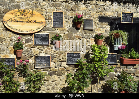 Restaurant La Casuca del Puente, durch eine Brücke über den Fluss Deva in Potes, Picos de Europa mit einer attraktiven Darstellung von Blumen und Menüs Stockfoto