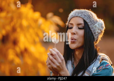 Porträt der jungen positive schönen Lächelnden jungen Frau bläst Löwenzahn im Herbst Park. Stockfoto