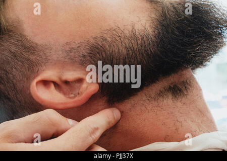 Ein junger gut aussehender bärtiger Mann in einem Friseursalon. Der Friseur zeigt, wie die Haare zu schneiden. Stockfoto