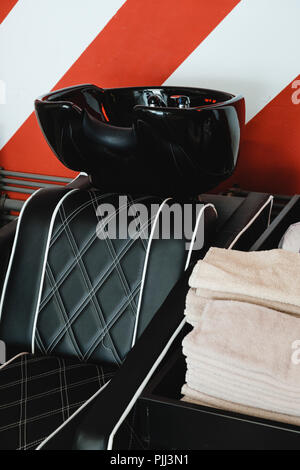 Zwei schwarze Ledersitze mit Waschbecken in einem barbershop Interieur mit Handtücher und Shampoo auf der Seite. Rot-weißen Streifen an der Wand. Stockfoto