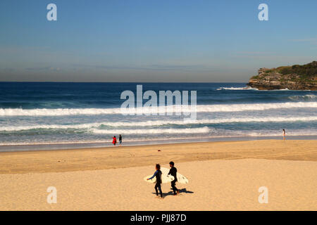Natürliche Sandstrand in Sydney, riesige Wellen und zwei Surfer gehen mit ihren Surf zum Wasser, Pazifischer Ozean, Bondi Beach in Australien Stockfoto
