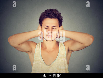 Junger Mann, die Ohren und die Augen geschlossen, die Vermeidung von Lärm auf grauem Hintergrund Stockfoto