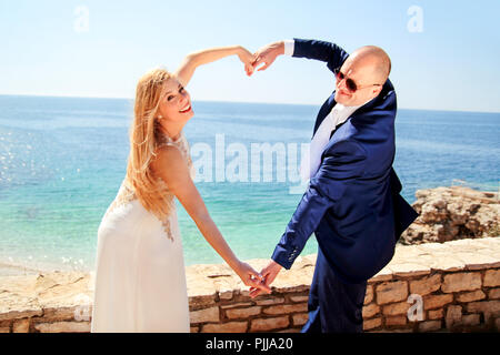 Hochzeit. Hochzeit Ehepaar der Hände machen ein echtes Herz. Glückliches Paar tag Hochzeit. Schöne Braut und Bräutigam am Strand. Fröhliches Ehepaar. Stockfoto