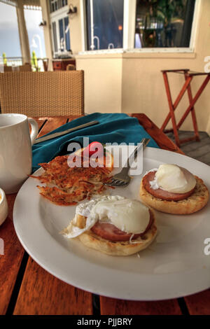 Pochierte Eier, kanadischer Speck, Sauce Béarnaise, und Rösti zum Frühstück mit Blick auf den Ozean. Stockfoto