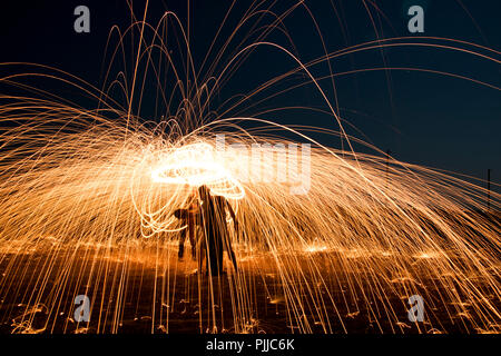 Paar tanzen mit Funken des Feuers fliegen in der Luft. Künstlerische Stahlwolle Feuer Malerei. Stockfoto