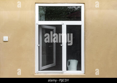 Ein geöffnetes Fenster mit Moskitonetz in der Wand des Hauses Stockfoto