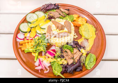 Gemischte Poke Salat auf einem weißen Holztisch. Die gesunden Salat auf einer runden Platte hat eine Thunfisch und Reis mit Cumcumber, Salat, Zwiebel, Mango, Karotte ein Stockfoto