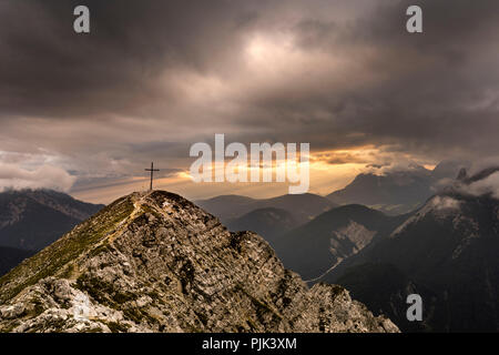 Gipfel der Brunnsteinspitze (2179 m) mit Gipfelkreuz und im Hintergrund Licht Stimmung in Tirol, von dramatischen Cloud Atmosphäre gerahmt, Stockfoto