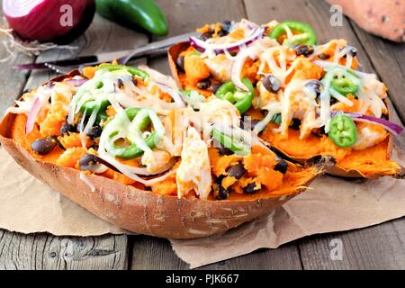 Gebackene süsse Kartoffeln gefüllt mit Hühnerfleisch, Gemüse und Käse, auf einem rustikalen, mit Holz Hintergrund schließen Stockfoto