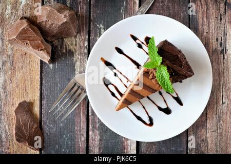 Stück Schokolade Käsekuchen auf Platte, oben Blick über eine rustikale Holz Hintergrund Stockfoto