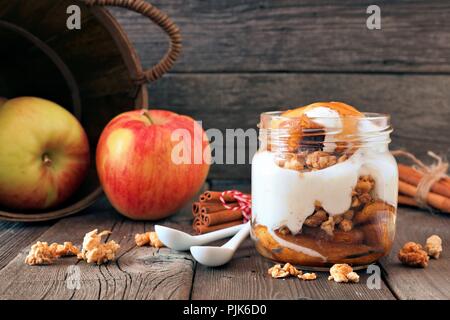 Herbst Bratapfel Parfait mit Karamellsauce in einem Marmeladenglas, noch Leben auf eine rustikale Holz Hintergrund Stockfoto