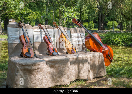 Musik und Natur Konzept. Saiteninstrumente, ein Cello und drei Violinen auf der zeremoniellen Stühle in der Natur. Close Up. Stockfoto