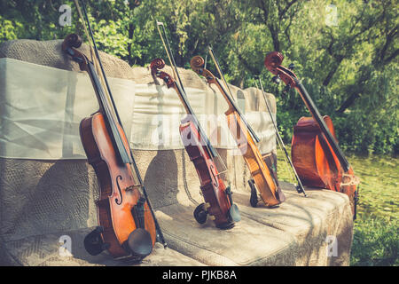 Musik und Natur Konzept. Saiteninstrumente, ein Cello und drei Violinen auf der zeremoniellen Stühle in der Natur. Close Up. Stockfoto