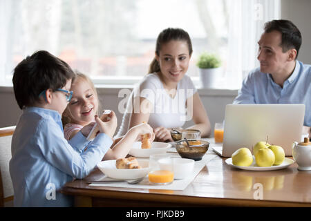 Glückliche Eltern beobachten begeistert Kinder spielen auf dem Smartphone in der Küche Stockfoto