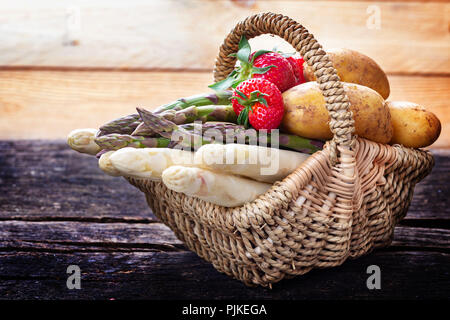 Spargel, Erdbeeren und Kartoffeln im Warenkorb auf Holz Stockfoto