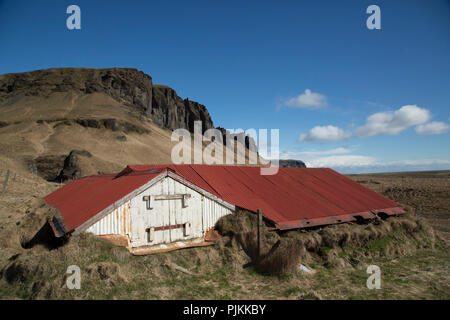 Island, South Island, alte Scheune im Gras, rot Blechdach, Berge, blauer Himmel Stockfoto