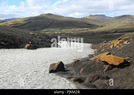 Island, zwei Wanderer auf einem Schneefeld in der Lava Wüste, Berge im Hintergrund, schwarzer Sand und orange Steine Stockfoto