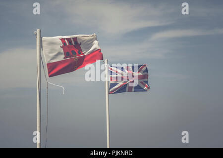 Zwei Fahnen, den Union Jack und unter der Flagge von Gibraltar, Seite an Seite weht im Wind vor blauem Himmel Stockfoto