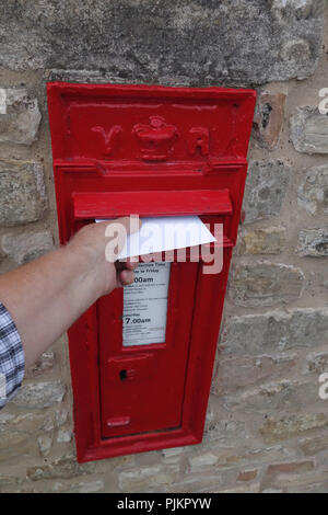 Mans Hand, Letter in einem englischen Dorf Post Box, die in großen Mauer aus Stein gebaut ist Stockfoto