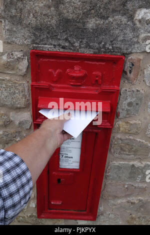 Mans Hand, Letter in einem englischen Dorf Post Box, die in großen Mauer aus Stein gebaut ist Stockfoto