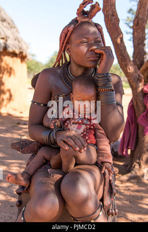 Himba Frau sitzt im Schatten eines Baumes mit Baby in ihren Armen Stockfoto