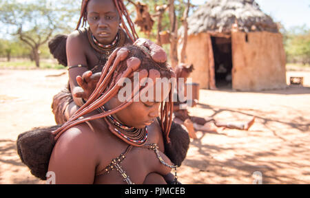 Junge Himba Frauen machen sich gegenseitig das Haar. Die Ocker-beschichtete Haar der Frauen ist zu Zöpfen verdreht Stockfoto