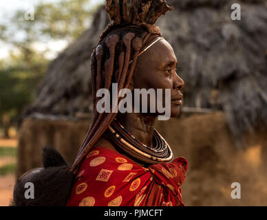 Porträt einer Frau Himba im letzten Sonnenlicht, Seite Profil. Das Baby auf dem Rücken ist gerade noch sichtbar Stockfoto