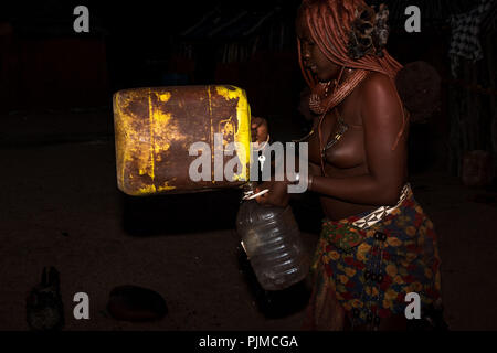 Junge Frau Himba gießen gesammelte Regenwasser, eine Seltenheit in Namibia, von einem Behälter in einer Kunststoffflasche Stockfoto