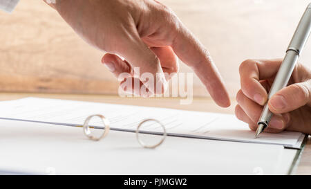 Männliche Hand deutete auf eine Scheidung Papier, auf dem eine Frau besetzt ist das Schreiben mit einem Stift in der Nähe zu konzeptionellen anzeigen. Stockfoto