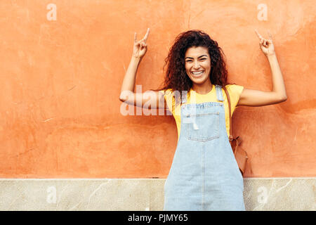 Lustige schwarze Frau mit schwarzen Locken Frisur im Freien. Arabische Mädchen in Freizeitkleidung in der Straße. Gerne weibliche tragen gelbe T-Shirt und Jeans Kleid Stockfoto