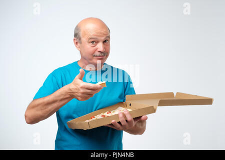Portrait von reifen europäischen Mann isst ein Stück Pizza. In seinen Händen hält er einen Karton mit Lebensmitteln. Studio shoot Stockfoto