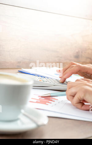 Nahaufnahme von weiblichen Händen, mathematische und statistische Berechnungen auf Weiß Tischrechner beim Korrekturlesen der Graphen mit einer Tasse ho Stockfoto