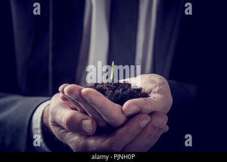 Retro Vintage Style Bild eines Kaufmanns Holding eine Pflanze wächst in den reichen Boden legte in seinen Händen in der Nähe zu sehen, konzeptionelle Bild. Stockfoto